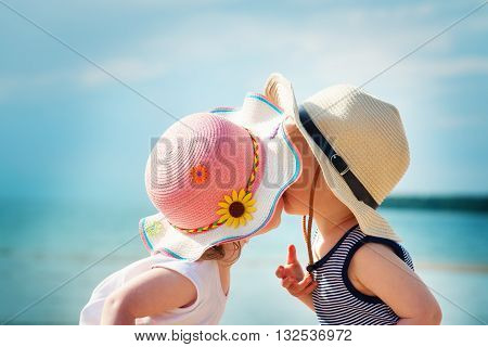 Babygirl and babyboy kissing on the beach in straw hats