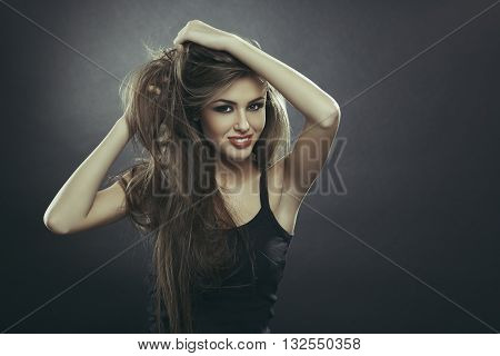 Beautiful sensual young lady posing with her hands through her long smooth healthy brown hair over dark grey background with copy space. Hair health hair freshness hair care.