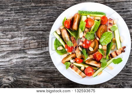 Grilled pork chops salad with tomatoes cucumber spinach peanuts garnished with cilantro served on white plate top view