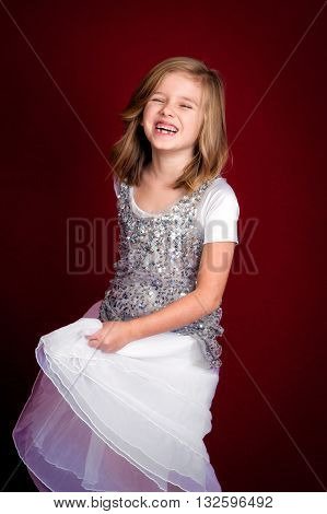 Portrait of a laughing blond haired girl swishing her dress. She is missing two teeth and looks extremely happy.