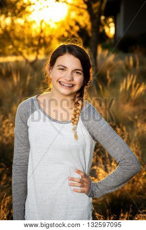 A teenage girl poses for a portrait. Hand on hip a bit slouchy backlit field in late afternoon sunlight.