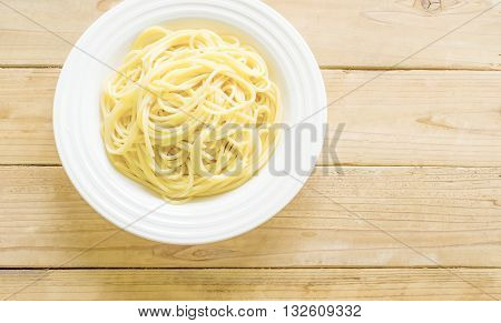 The spaghetti in a white plate on a wooden table.