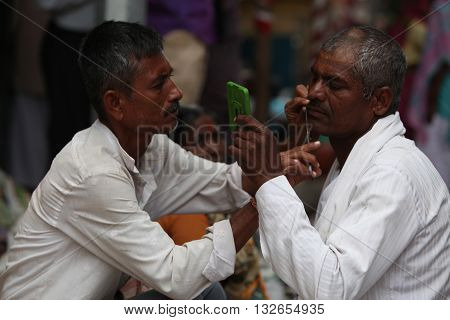 Pune India - ‎July 11 ‎2015:A streetside barber shaves a pilgrim during a huge pilgrimmage in India
