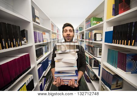 Student holding lot of books in school library. Hard worker and persistence concept.