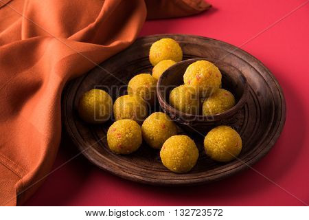 Indian sweet bundi laddu or motichur laddu served in a carved woodel bowl and plate with drapery or table napkin, selective focus