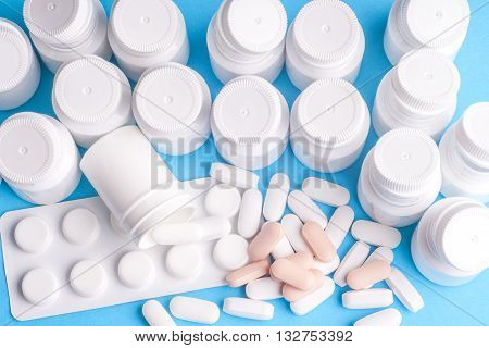 Many pills and tablets isolated on light blue background. Pharmaceutical medicament cure in container for health. Antibiotic painkiller closeup. Copy space for text.