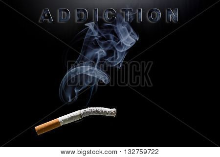 Burning cigarette smoke and text addiction on black background
