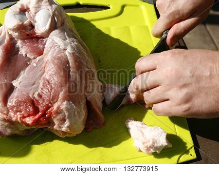 A large piece of pork. Man cuts it up into little pieces.