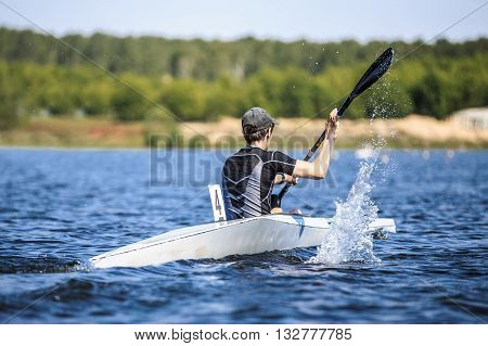young man athlete on rowing kayak on lake during competition