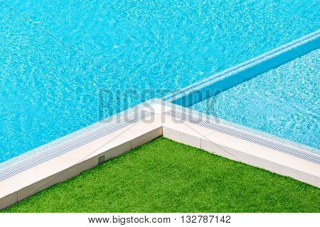 Corner of swimming pool with green grass around.Hotel swimming pool with sunny reflections close up view.Swimming pool with green grass around.