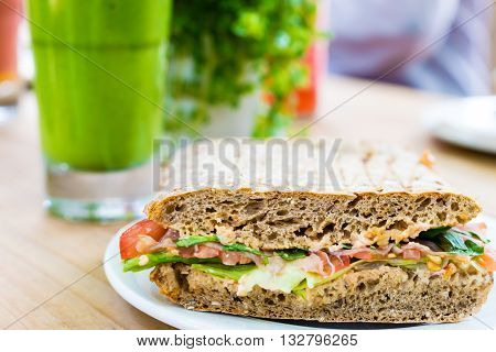 Sandwich with ham, tomato, rucola und salad serviert with smoothie on wooden table.