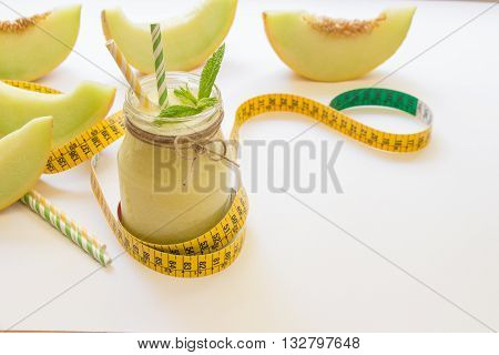 Left a jar with melon smoothie near cut slices of melon centimeter straws right empty place for text on a white background. Melon smoothie in a jar. Horizontal. Daylight.