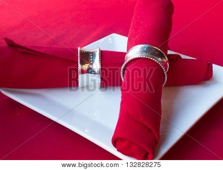 Red napkin in silver holder on a white plate