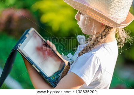Young Caucasian Girl Playing with Tablet Device in the Garden. Closeup Photo