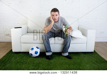 crazy football fan cheering watching television soccer match suffering stress nervous and excited sitting on sofa couch with grass carpet and ball emulating stadium pitch