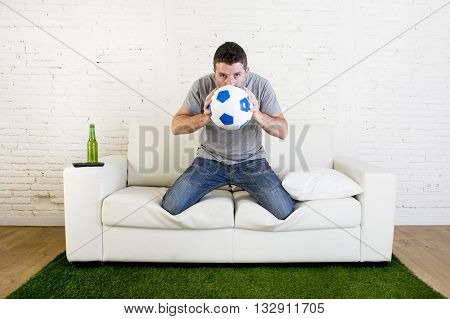 crazy football fan cheering watching television soccer match suffering stress nervous and excited kissing the ball hoping luck on sofa couch with grass carpet emulating stadium pitch