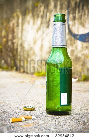 Bottle of beer resting on the ground with three cigarette's butts. Alcoholism and tobacco addiction concept
