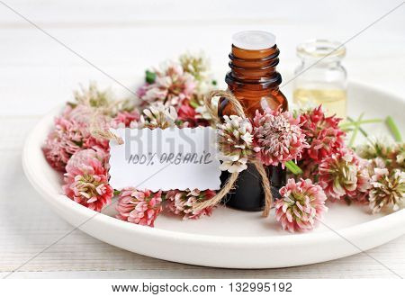 Cosmetic bottle of aroma oils extract, clover flowers, paper tag handwritten text organic. Herbal skincare.