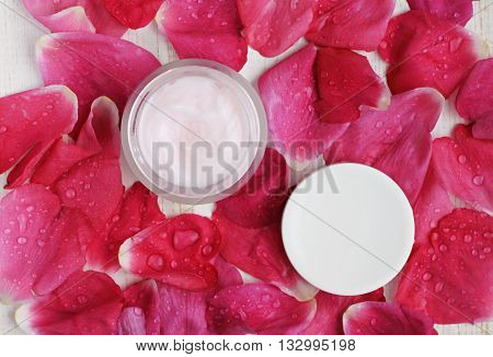 Cosmetic cream container, top view, rose petals water drops scattered background. Aromatic skin care balm.