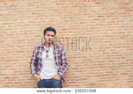 Young Handsome Hipster Man Wearing Plaid Shirt And Jeans Against A Brick Wall.