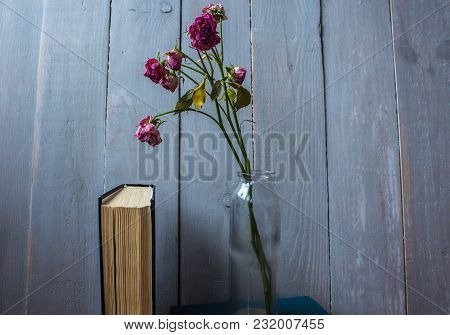 Roses In A Bottle And A Book On Wooden Background