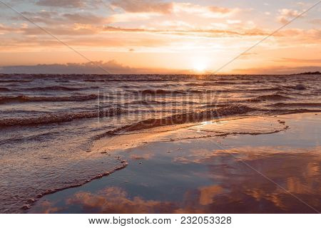 Horizontal Shot Of The Wave At Sunset Lapping On A Sandy Beach Against The Sea In Blur. Tonted Orang