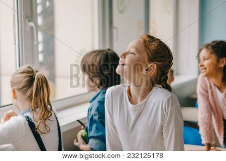 Adorable Schoolchildren Looking At Window Together At Classroom