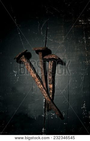 high angle view of three rusty nails, depicting the nails of the holy cross, on a rustic wooden surface, with a dramatic effect