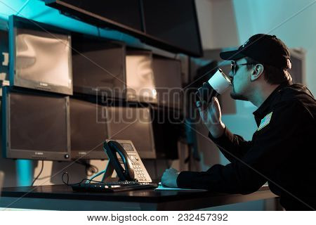 Prison Guard Drinking Coffee At Workspace And Monitoring People In Jail