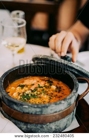 National Cuisine Of Cape Verde: Cachupa In Traditional Stone Bowl. White Wine Glasses In Background.
