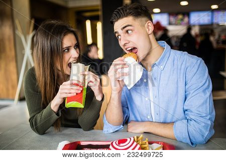 Young Couple In A Fast Food Restaurant Eating Hamburger And Doner