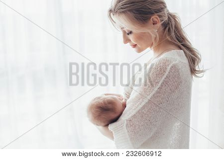 Bright portrait of a mom breast feeding baby over window lighting.
