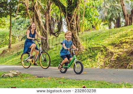 Happy Family Is Riding Bikes Outdoors And Smiling. Mom On A Bike And Son On A Balancebike.