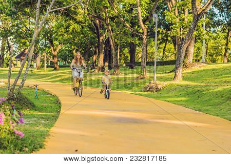 Happy Family Is Riding Bikes Outdoors And Smiling. Mom On A Bike And Son On A Balancebike.