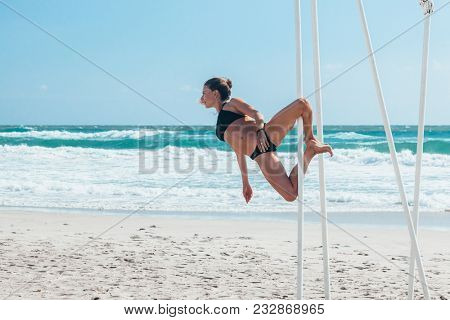 Pole dance outdoors. Young slim girl doing poledance on the beach over sea.