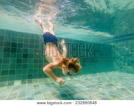 A Child Boy Is Swimming Underwater In A Pool, Smiling And Holding Breath, With Swimming Glasses.