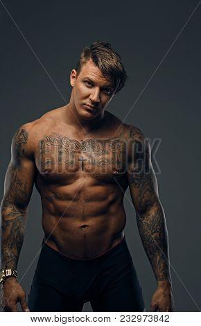 Studio Portrait Of Tattooed Muscular Male In A Shadow Isolated On Grey Background.