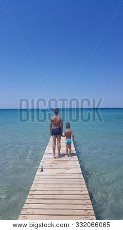 Wooden Pier On The Beach. Two Brothers Stand On A Pier In The Sea. Two Boys On A Pier By The Sea.