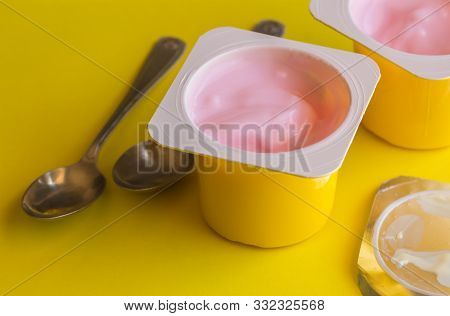 Two Strawberry Yogurt Cups With Small Silver Spoons On Bright Yellow Background - Pink Yoghurt Pots