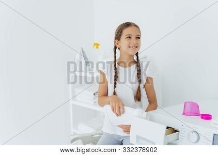 Little Happy Girl Has Two Pigtails Fills In Washing Machine With Liquid Detergent, Pours Into Tray O