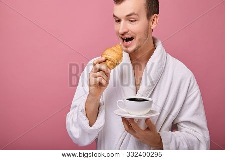 A Perky Guy In A White Bathrobe Is Standing On Wall Back With A Croissant In One Hand And A White Cu