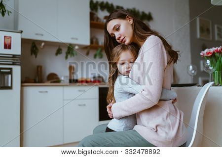 Mom Hugged Her Daughter In The Kitchen, Both Faces Have An Expression Of Quiet Sadness Or Sadness