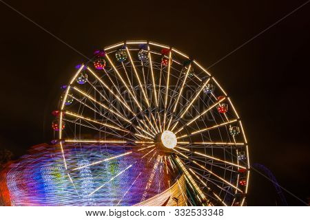 Two Rides In Motion In Amusement Park, Night Illumination. Long Exposure.