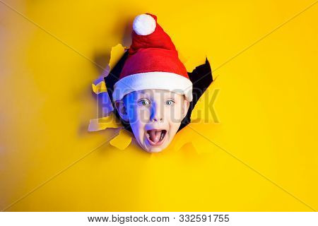 Little Cheerful Santa In A Hat Smiles, Getting Out Of The Ragged Yellow Background Lit By Neon Light