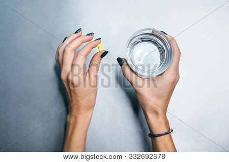 Hands Of Caucasian Girl With Yellow Pill In Left Palm And Glass Of Water In Right Hand. Pilule From 