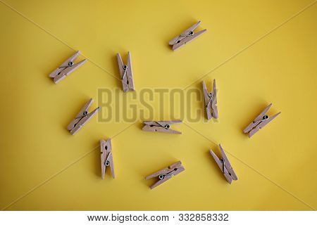 Many Wooden Clothespins Lie On A Yellow Background.