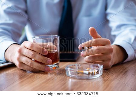 Male employee drinking alcohol and smoking cigarettes at workpla