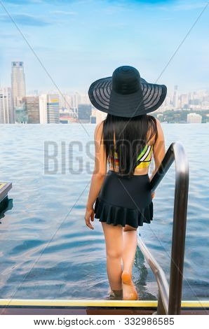 Young woman in a roof top swimming pool, infinity pool with beautiful city view. Vacation in Singapore.