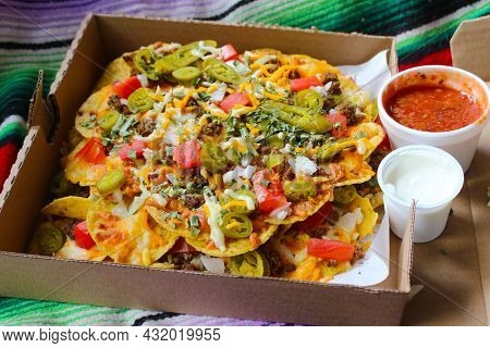 Take Out Box With Nachos Topped With Beef, Jalapenos,tomatoes, Onions And Cheese, With Salsa And Sou