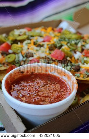 Take Out Box With Nachos Topped With Beef, Jalapenos,tomatoes, Onions And Cheese, With Salsa A On Th